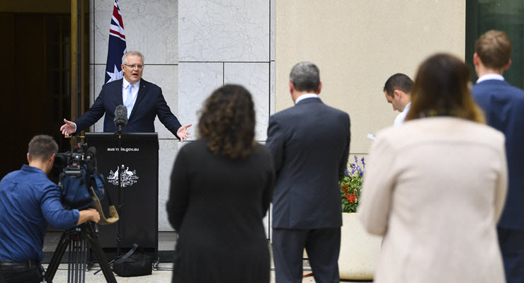 scott morrison stands behind a podium facing members of the press