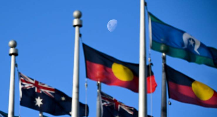 The Australian, Indigenous and Torres Strait Flags fly before the moon at Parliament (Image: AAP/Lukas Coch)