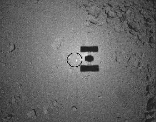 Hayabusa's shadow falls beside a circled reflective target it dropped as a guide for its sample recovery approach